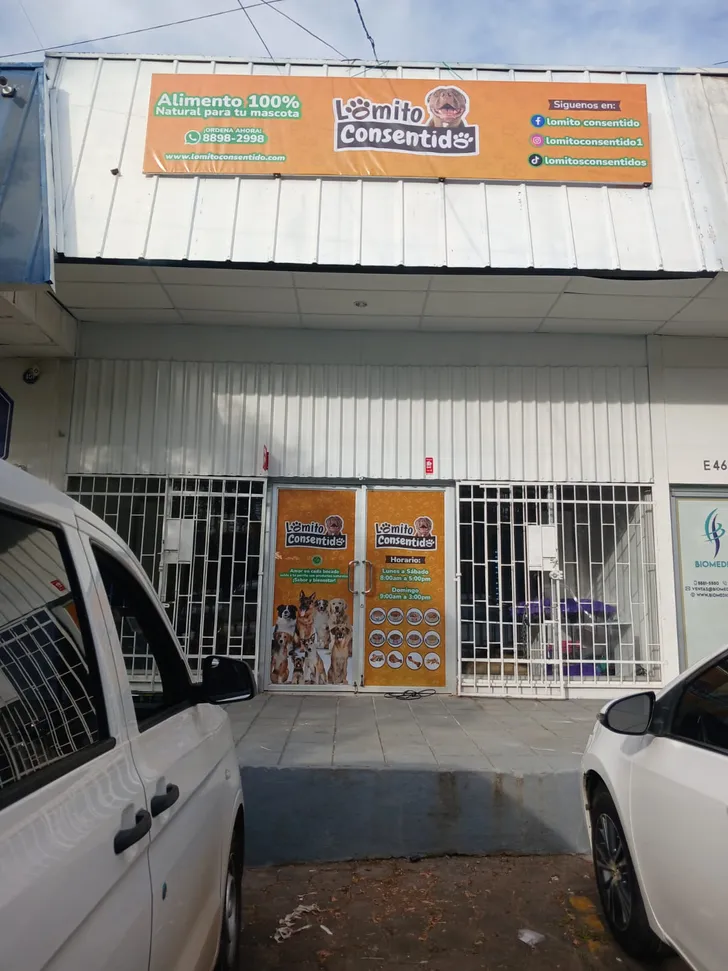 Fachada de tienda Lomito Consentido con banner naranja, horarios, contacto y promoción de alimento natural para mascotas.
